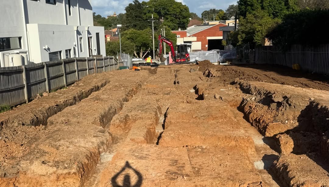 Service trenches on a site with an excavator working in the background